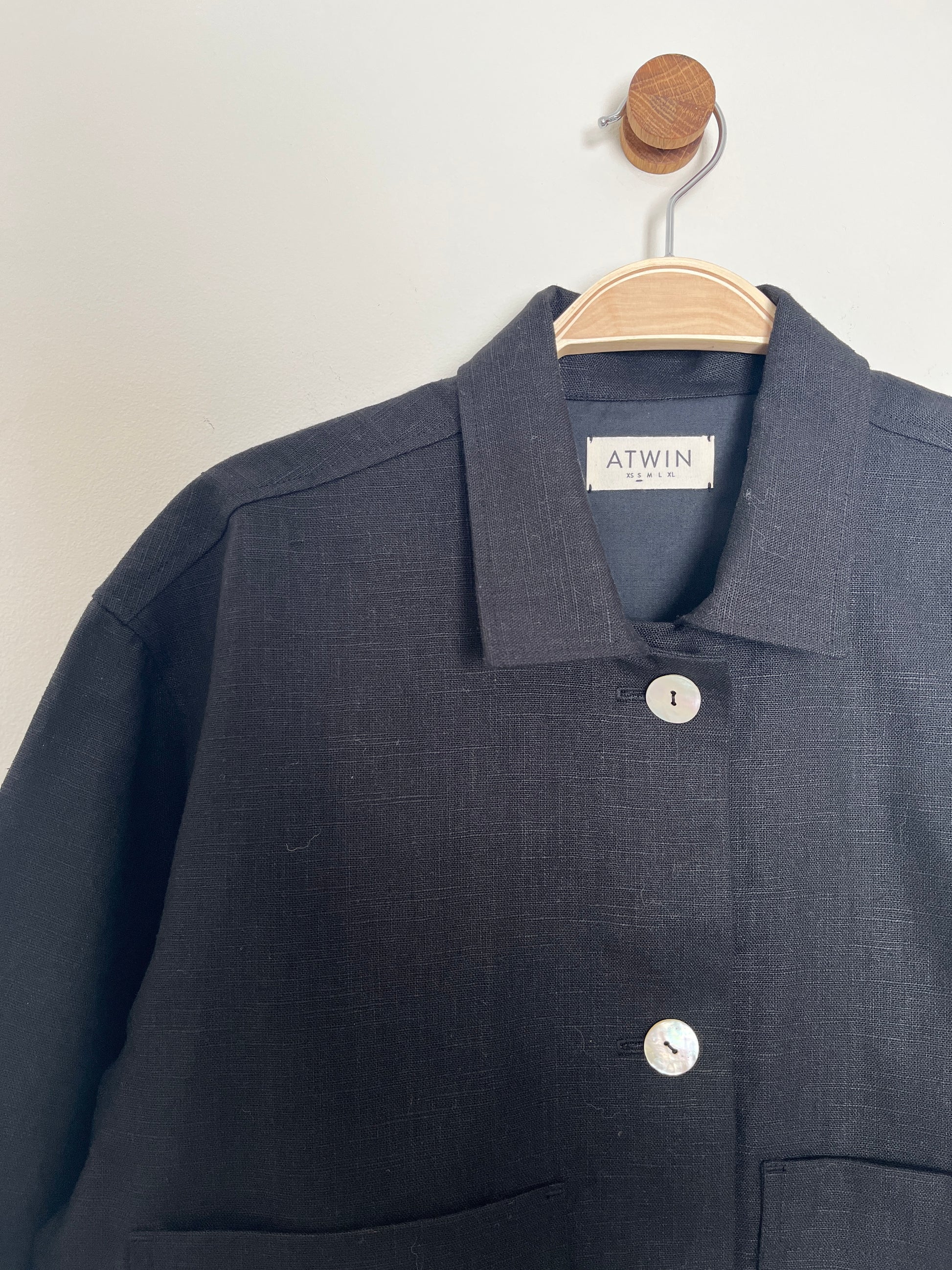 black workwear jacket with 'ATWIN' label on a wooden hanger against a white background