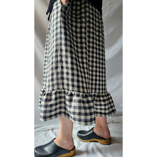 Person wearing a black and white checkered skirt with ruffled hem on a plain background