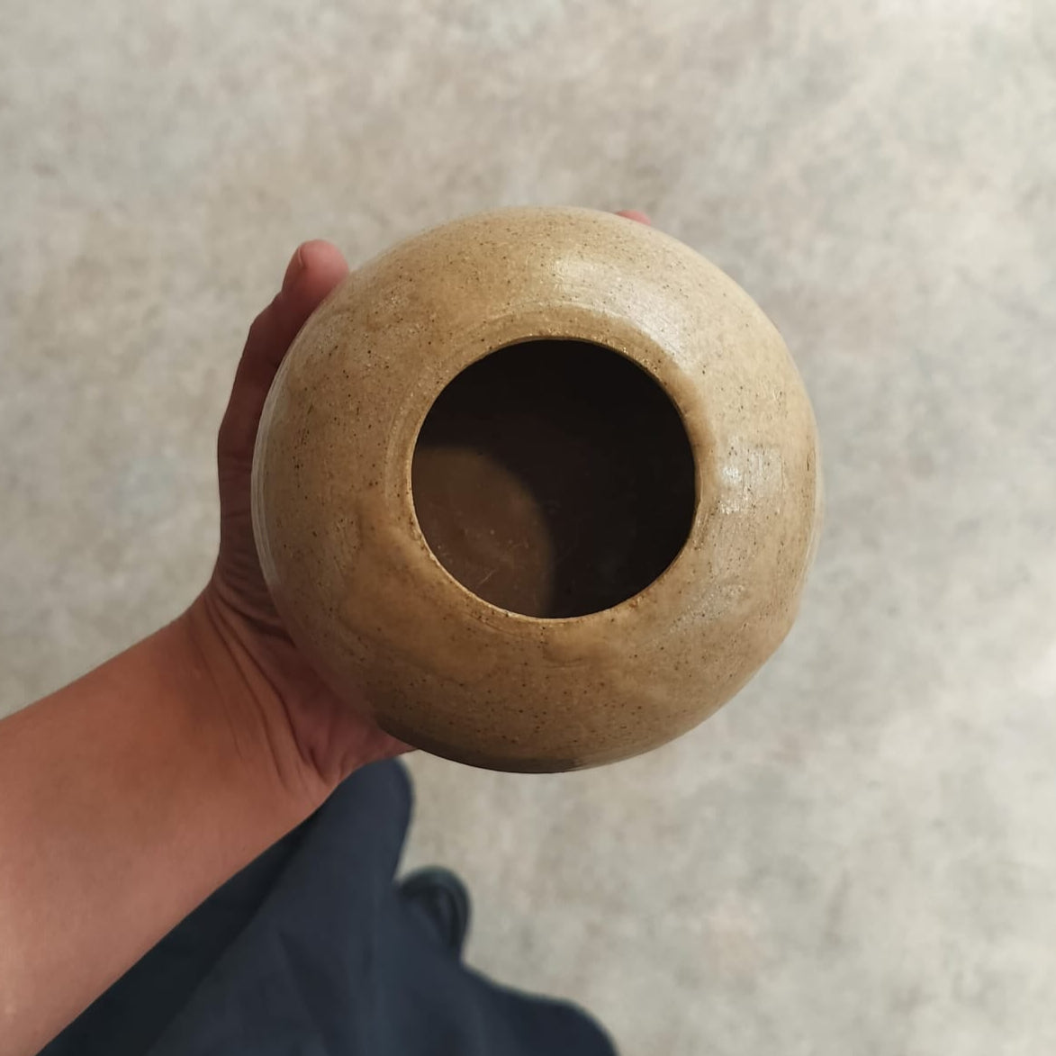 Hand holding a small brown ceramic pot against a neutral background