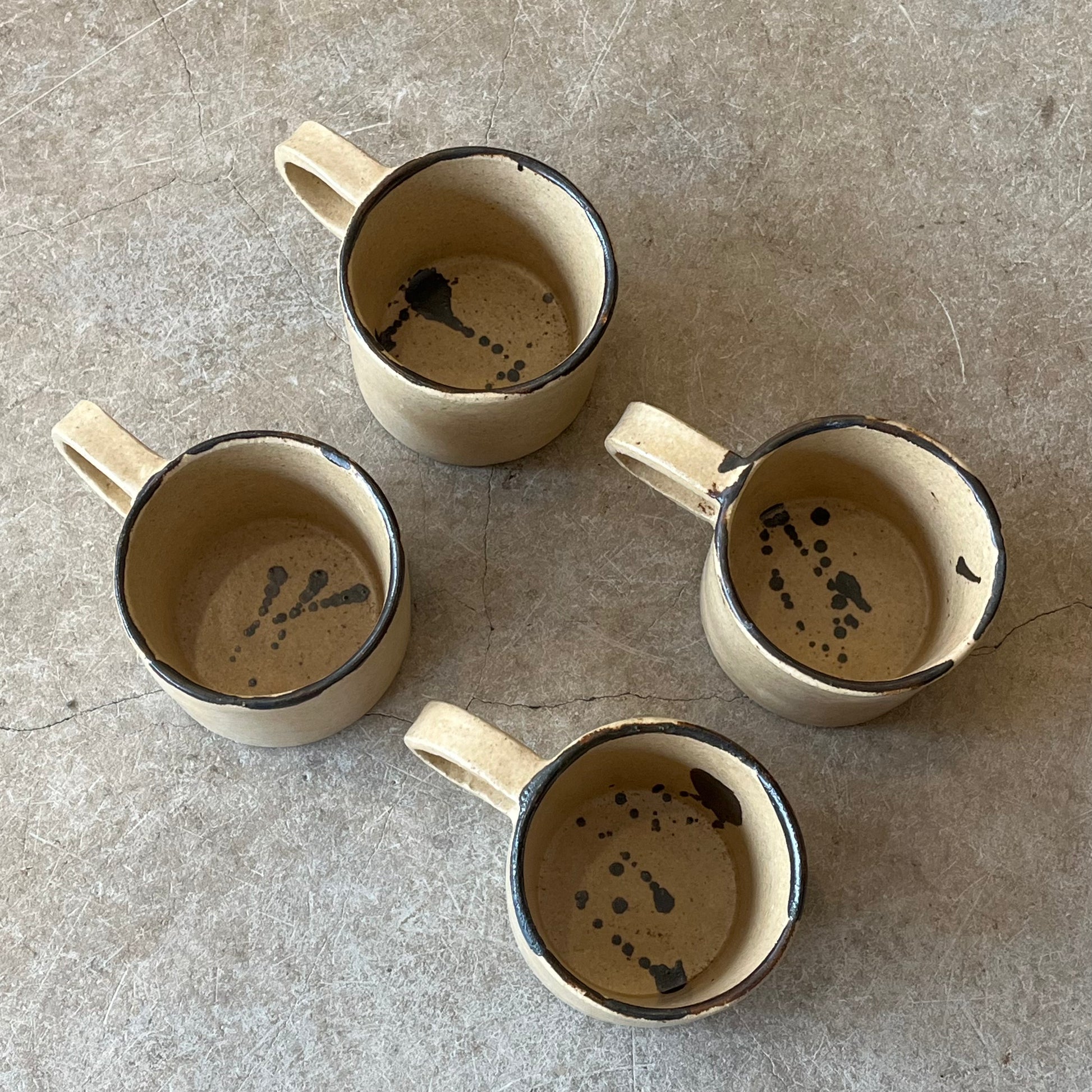 Four ceramic mugs with speckled interior design on a gray surface