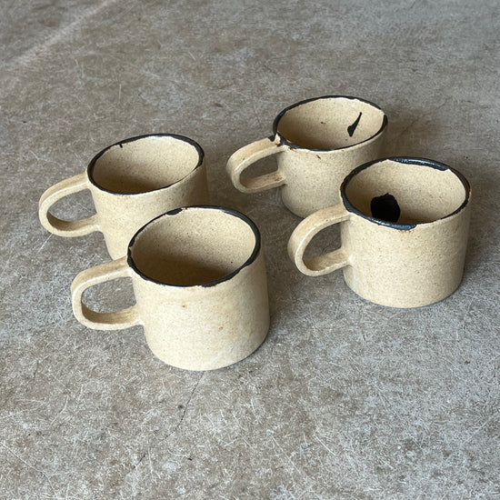 Four ceramic mugs with black interior on a gray stone surface