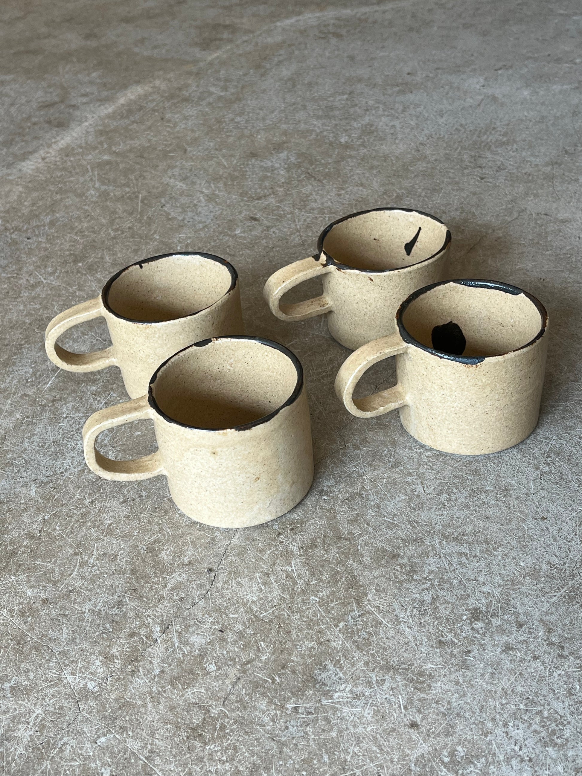 Four ceramic mugs with black interior on a gray stone surface
