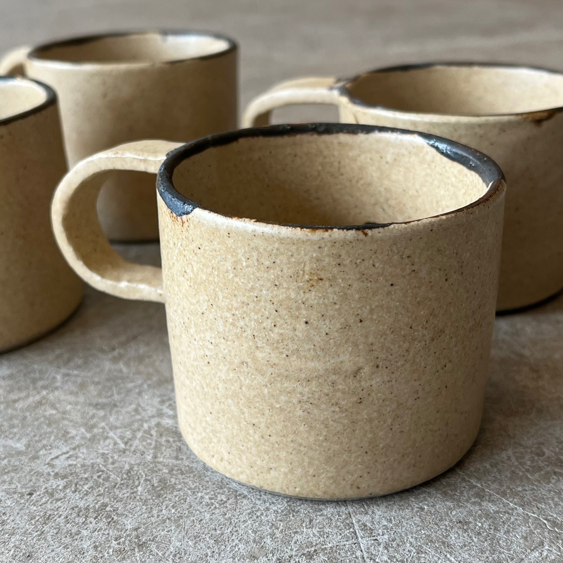 Set of beige ceramic mugs with black interior on a gray surface