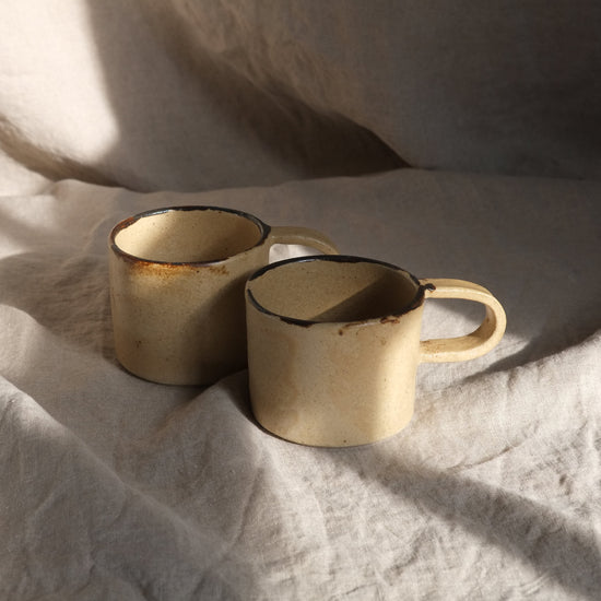 Two ceramic mugs on a textured white fabric surface