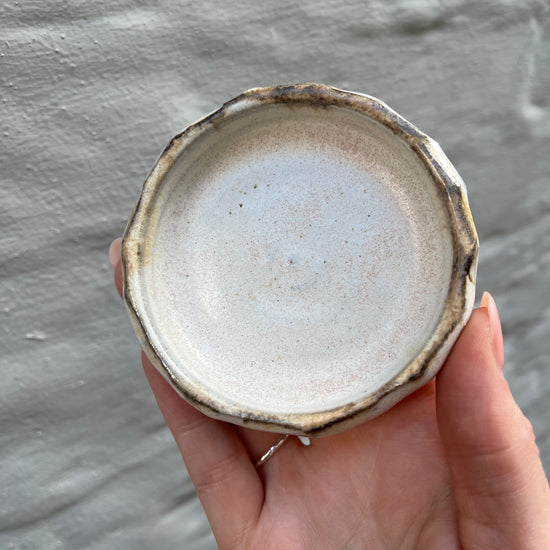 Hand holding a small ceramic dish with a textured surface against a gray background