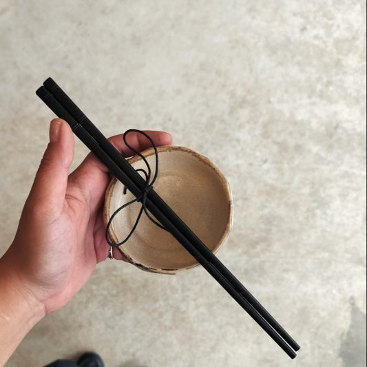 Hand holding black chopsticks over a beige ceramic bowl on a textured surface