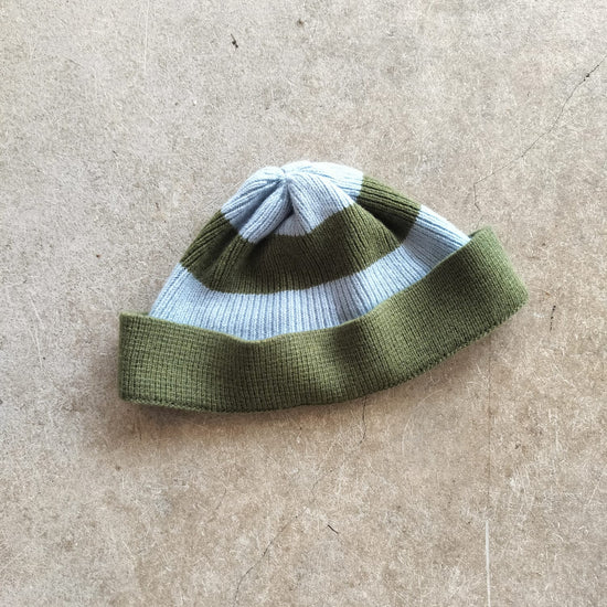 Knitted beanie with green and blue stripes on a beige surface