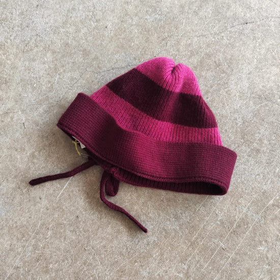 Maroon and pink striped knit baby hat on a beige surface