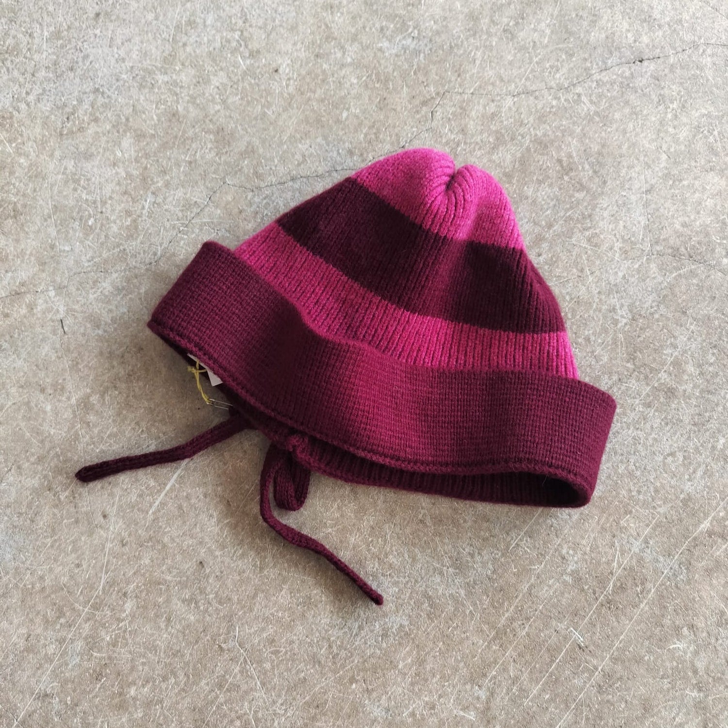 Maroon and pink striped knit baby hat on a beige surface