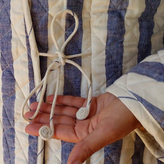 Hand holding a string against a blue and white striped fabric background