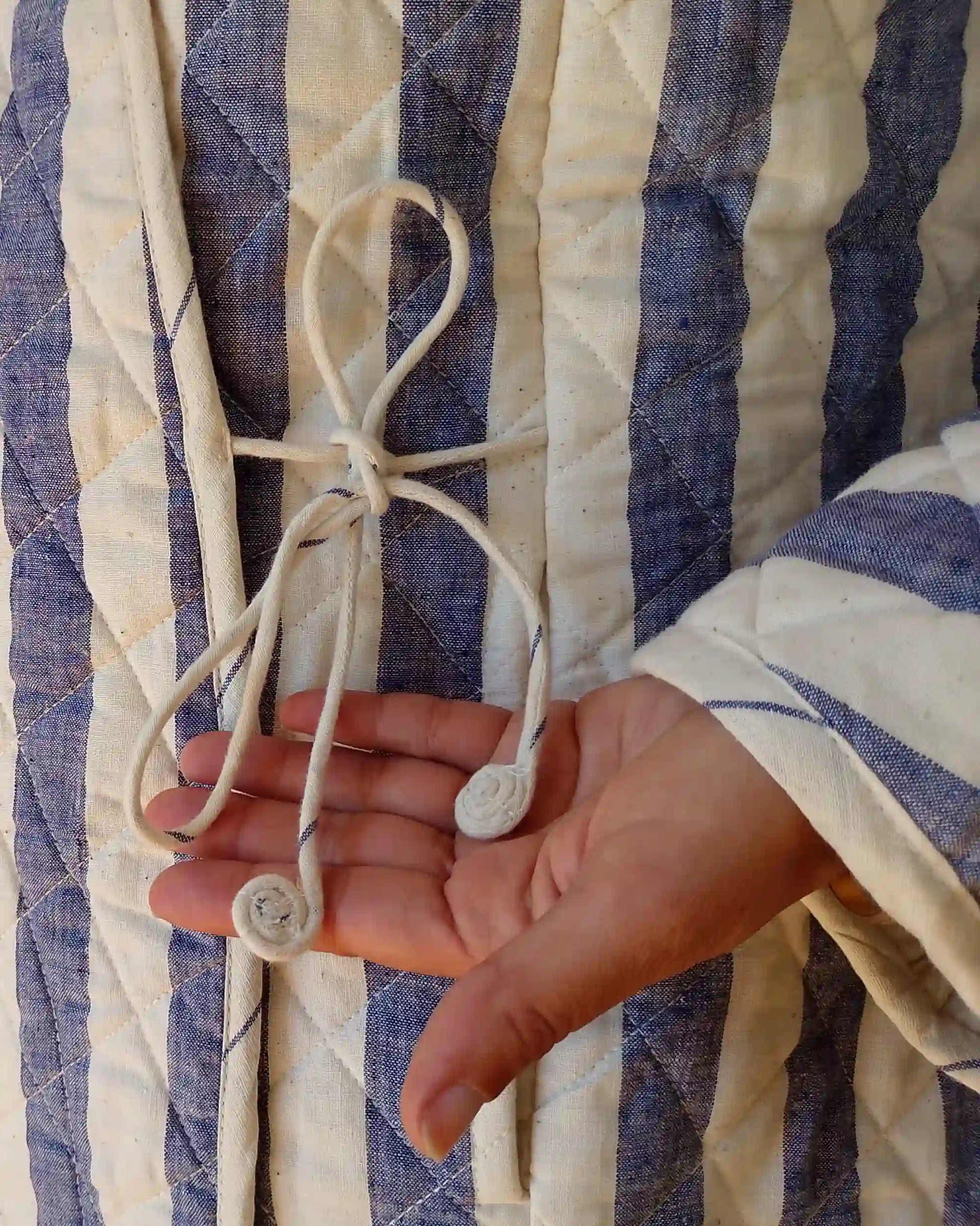 Hand holding a string against a blue and white striped fabric background
