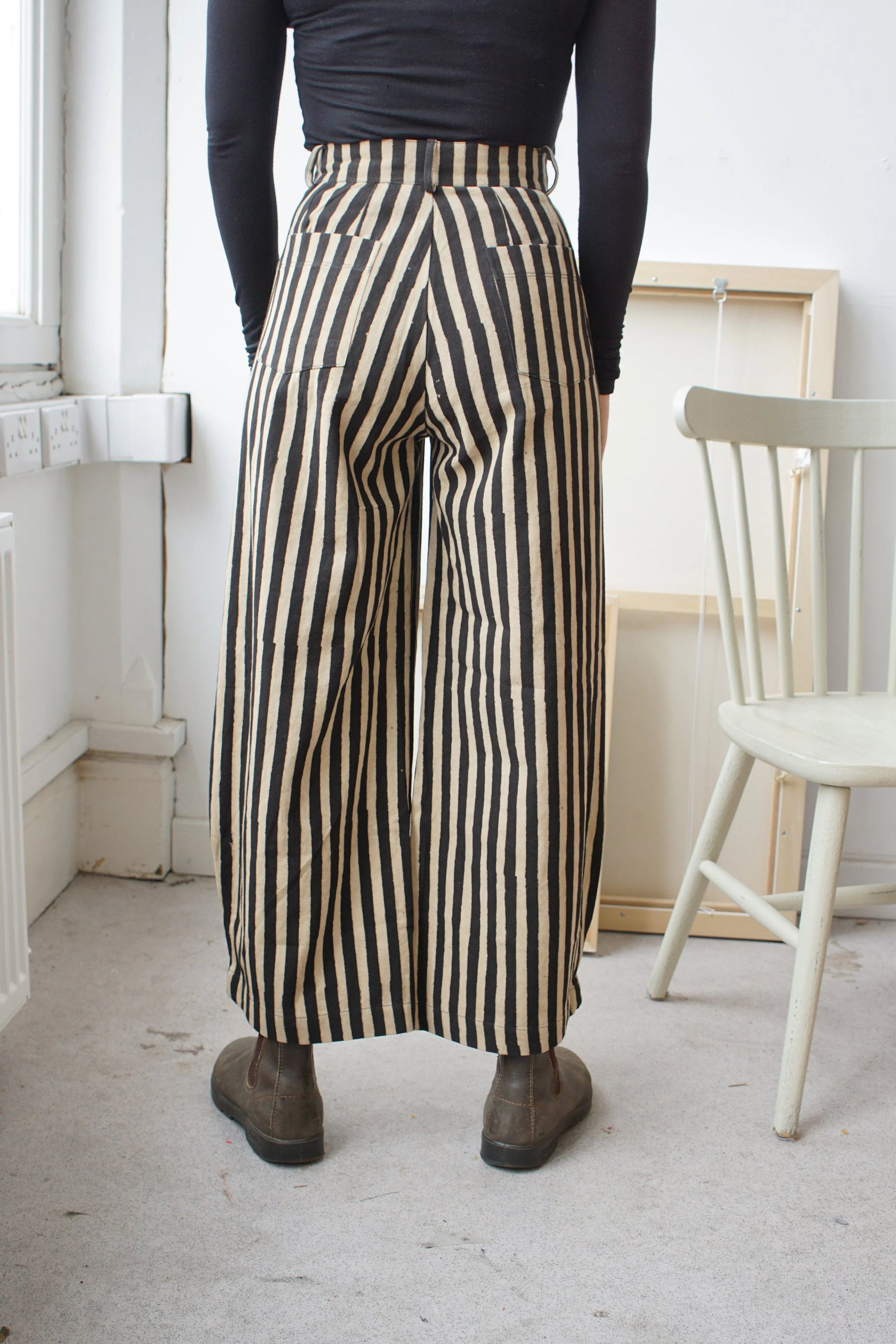 woman wearing long black and white striped trousers facing the wall