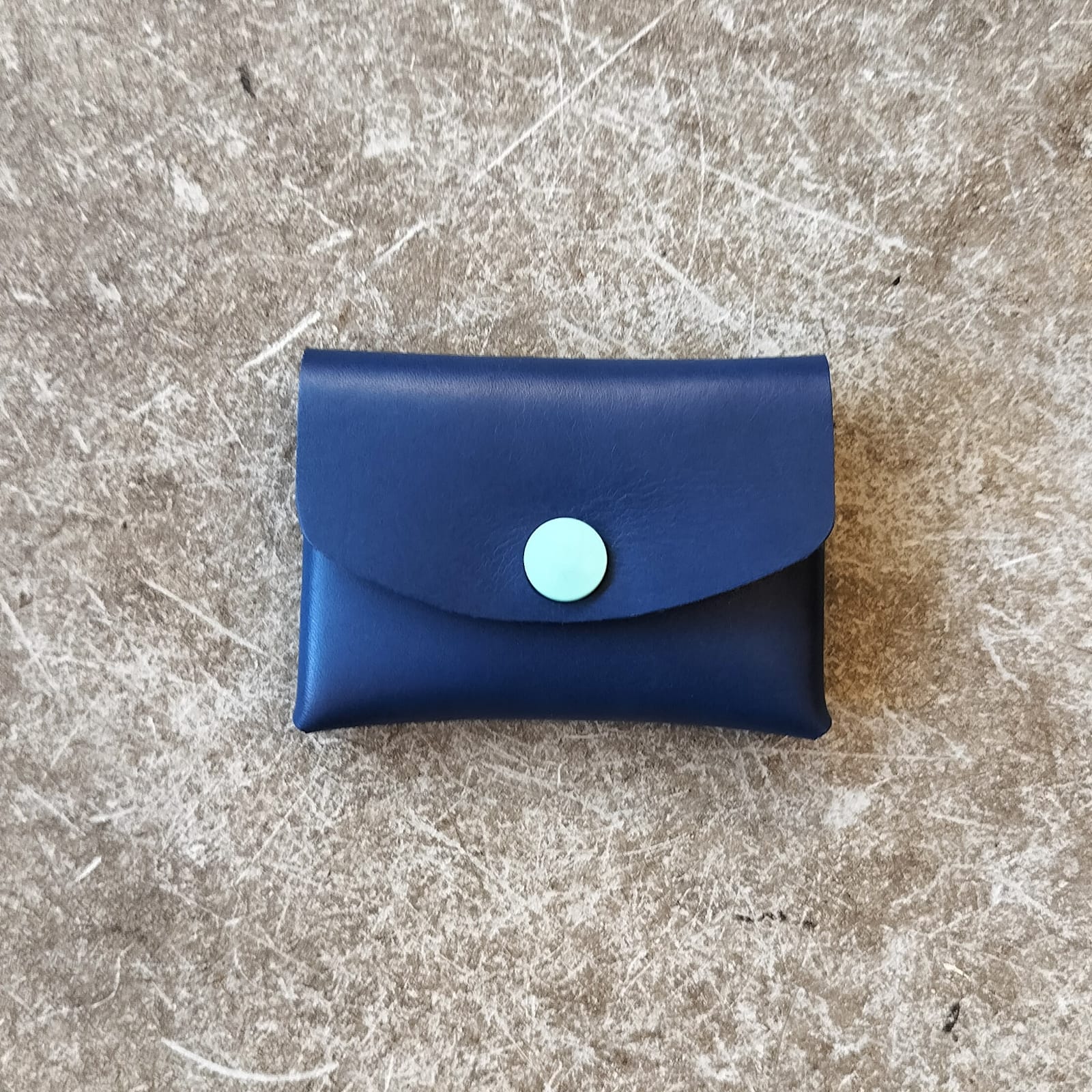 Blue leather wallet with a circular blue button on a textured gray surface