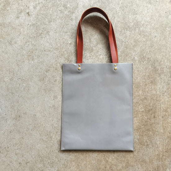 Grey tote bag with red leather straps on a textured beige surface