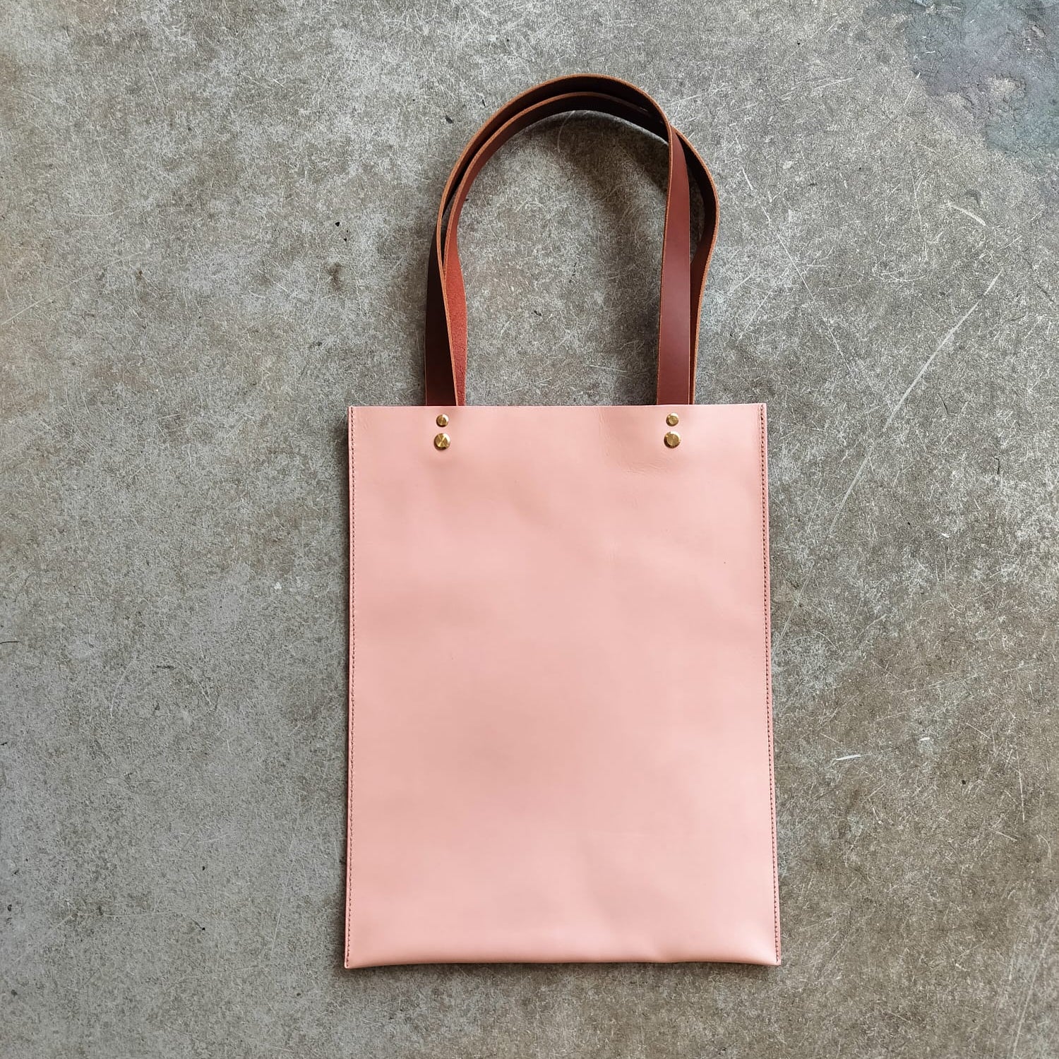 Pink tote bag with brown straps on a gray concrete surface