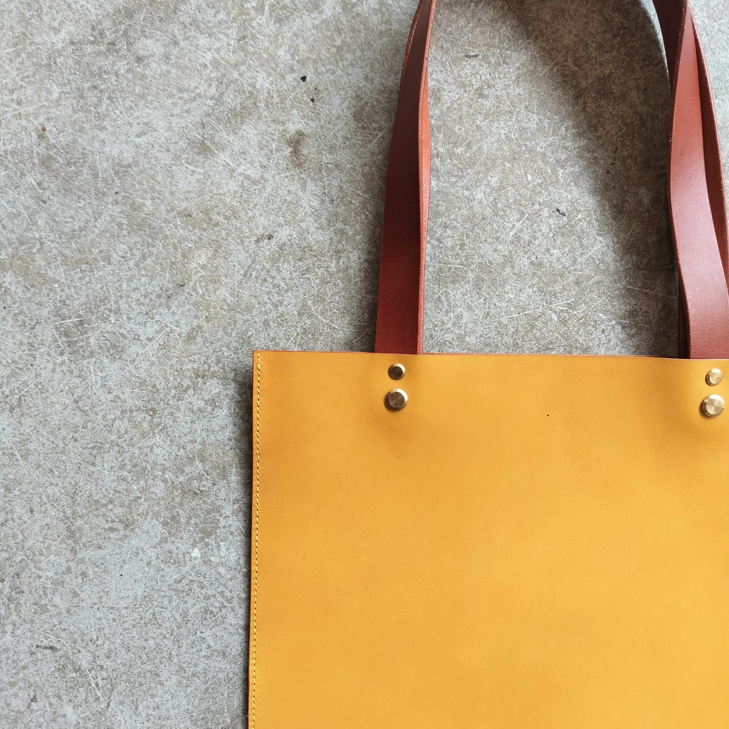 Yellow tote bag with red handle on a gray concrete surface