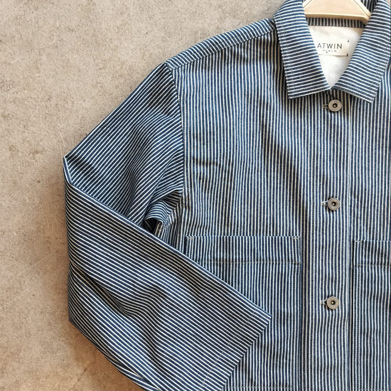 Blue and white striped workwear jacket on a hanger against a beige background