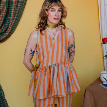 Woman wearing an orange and white striped outfit against a yellow wall.