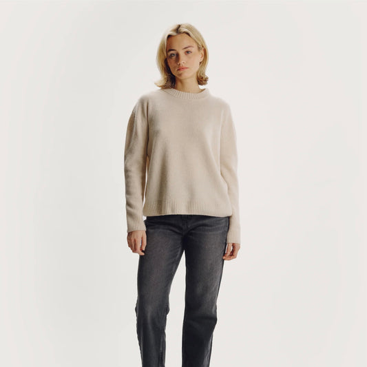 Model wearing a beige sweater and dark jeans on a plain background