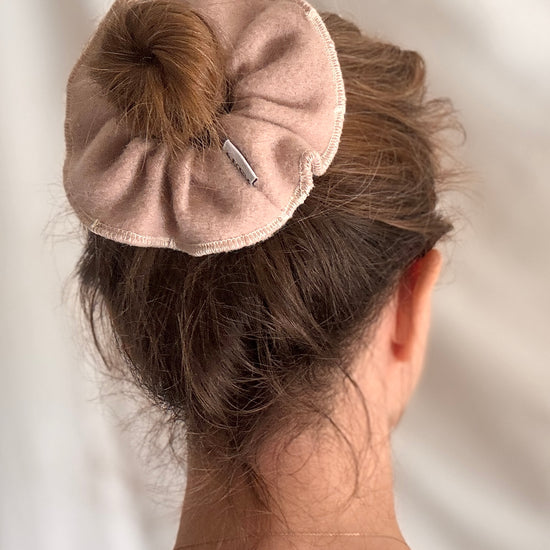 Person with a beige scrunchie in their hair against a neutral background