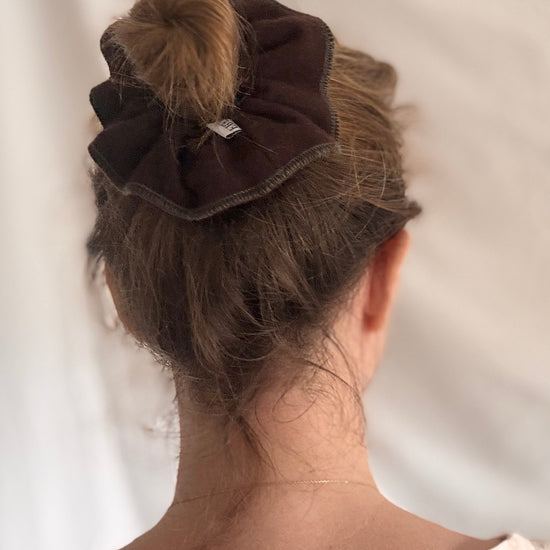 Brown scrunchie in a bun on a plain background