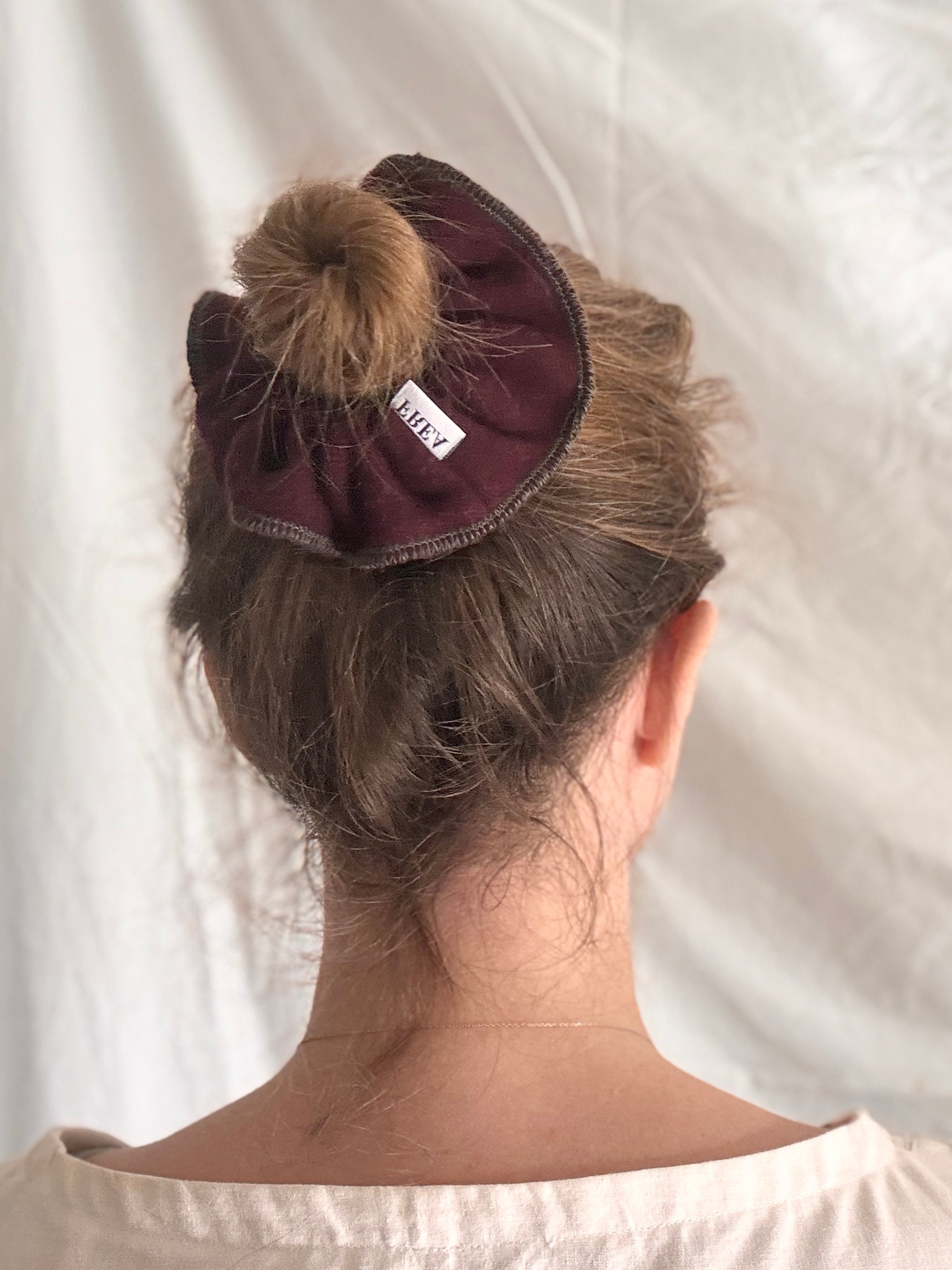 Person with a purple scrunchie in their hair on a white background