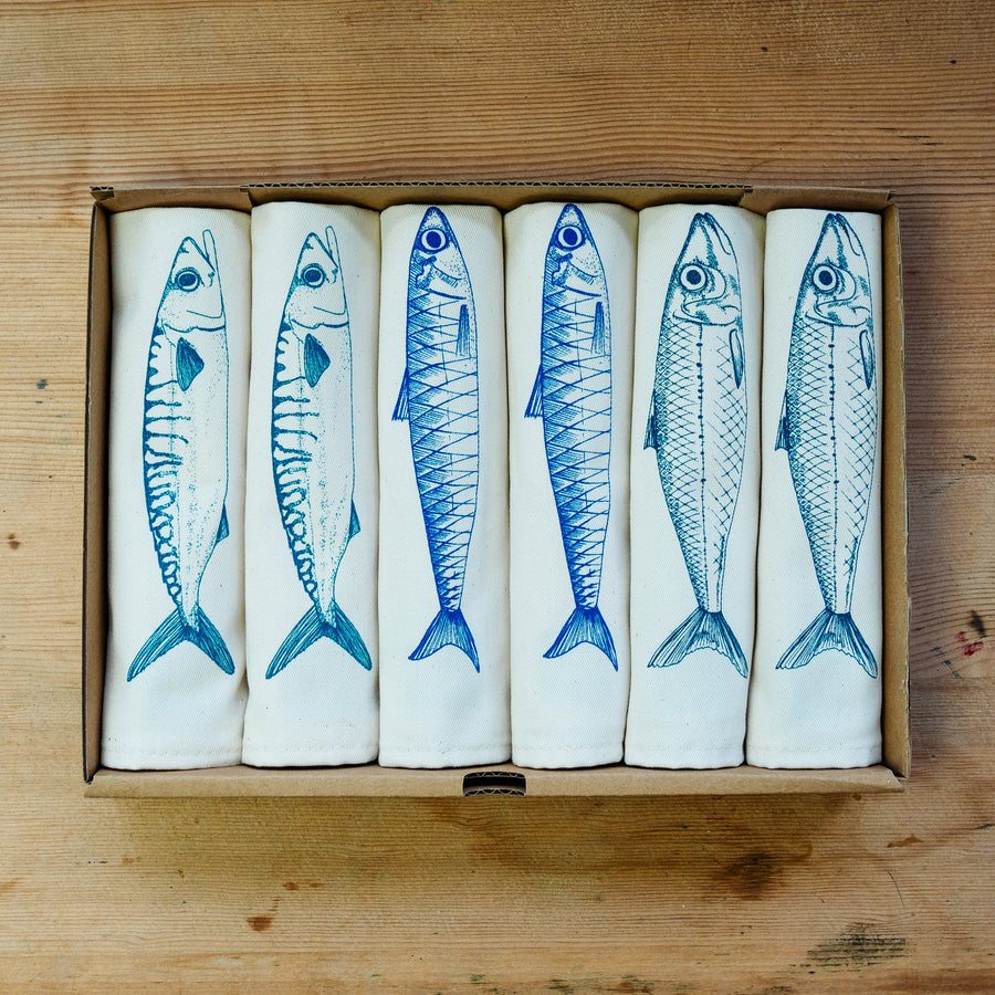 A set of white cotton napkins with blue fish prints, displayed in a giftbox.