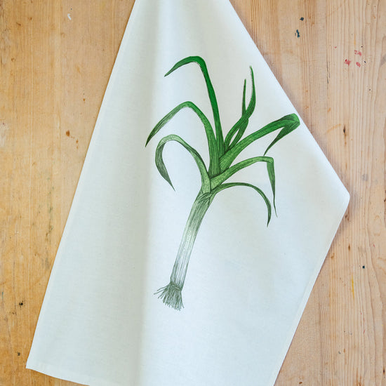 a leek illustrated tea towel on a wooden surface