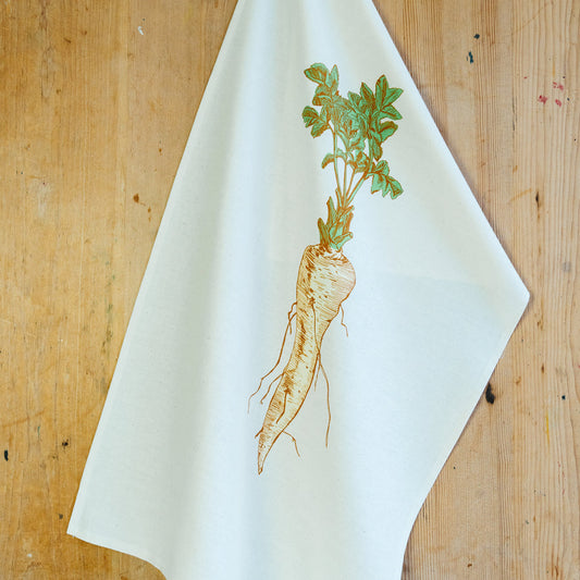 A parsnip illustrated tea towel on a wooden surface