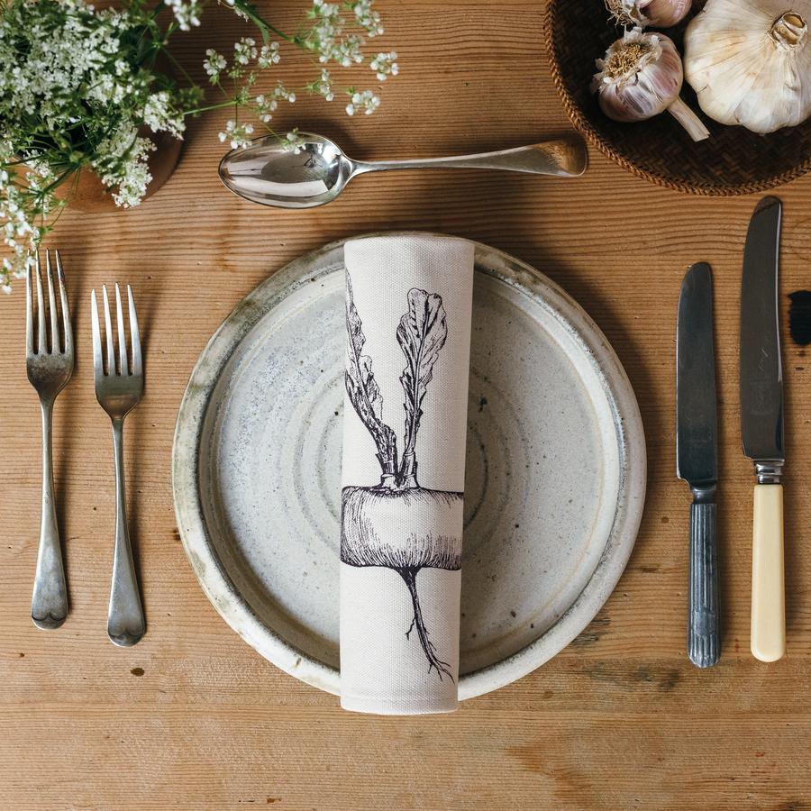Root vegetable printed napkin on a plate and laid table with cutlery and garlic