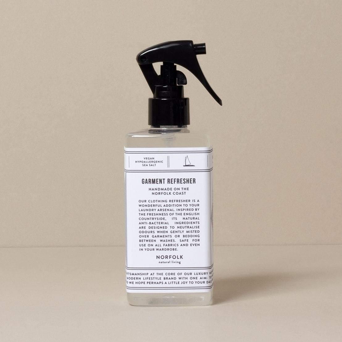 A clear bottle with a black spray pump labeled 'Garment Refresher' by Norfolk Natural Living, with Coastal Walks scent mentioned on the label.