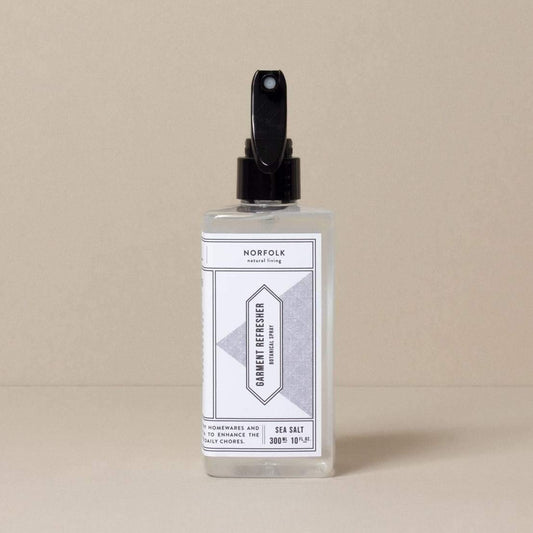 A clear bottle with a black spray pump labeled 'Garment Refresher' by Norfolk Natural Living, with Coastal Walks scent mentioned on the label.