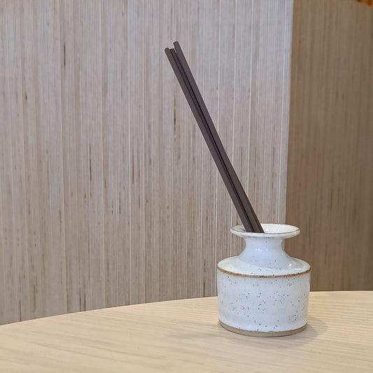 Ceramic diffuser with dark sticks on a wooden surface