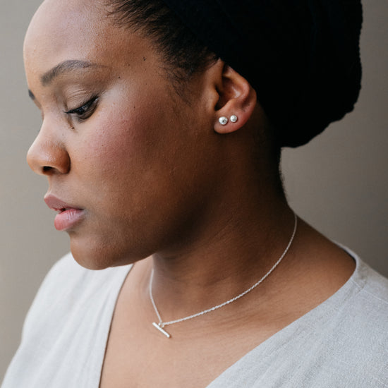 A silver bar necklace with a high polish pendant on a delicate trace chain, displayed on a model