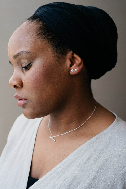 A silver bar necklace with a high polish pendant on a delicate trace chain, displayed on a model