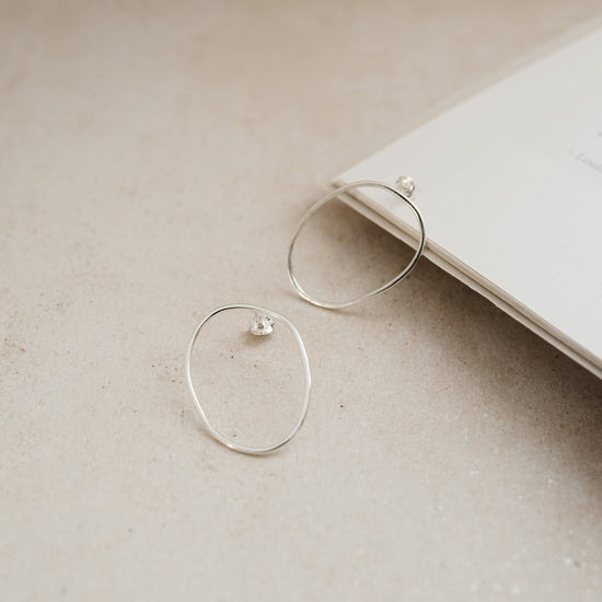 A pair of silver oval stud earrings placed on an open book.