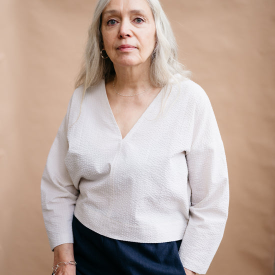 Woman wearing a white sweater and dark pants against a beige background