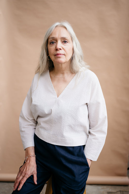Woman wearing a white sweater and dark pants against a beige background