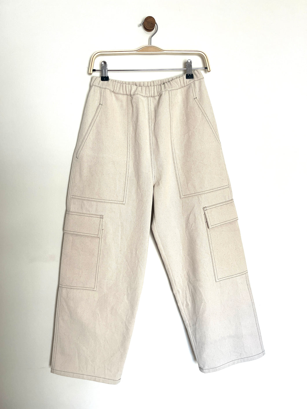 Ecru denim cargo trousers with two utility front pockets and two side patch packets with an elasticated waist band on a grey to white background