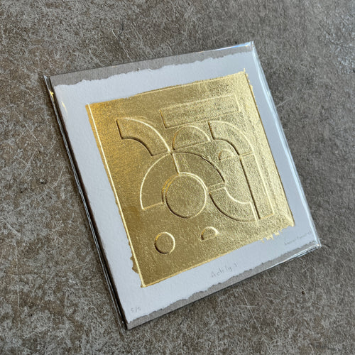 Gold leaf embossed geometric abstract print with a white boarder on heritage cotton paper. Square shaped on a grey concrete background
