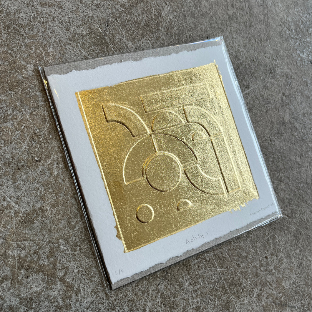 Gold leaf embossed geometric abstract print with a white boarder on heritage cotton paper. Square shaped on a grey concrete background