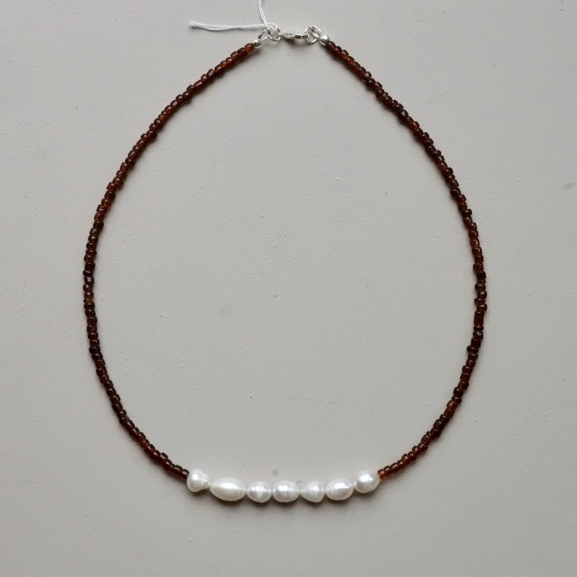 A beaded necklace featuring dark brown seed beads with a horizontal row of five white freshwater pearls across the center, finished with a silver clasp.
