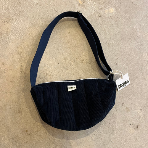 Navy blue padded corduroy cross body bag with adjustable strap and zip on grey concrete background
