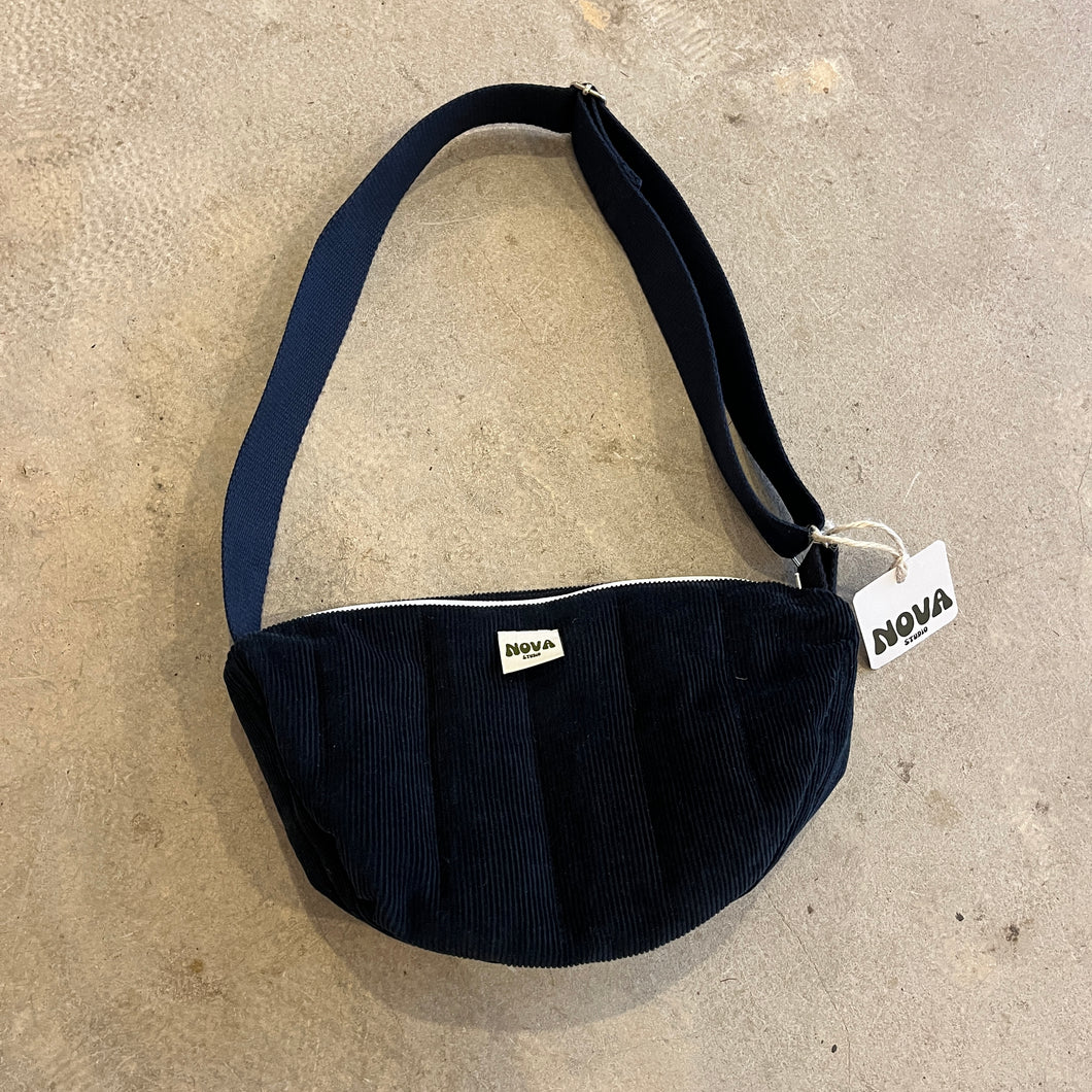 Navy blue padded corduroy cross body bag with adjustable strap and zip on grey concrete background