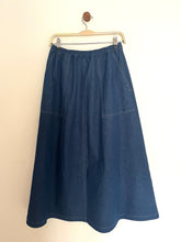 Load image into Gallery viewer, Indigo denim aline midi skirt with an elasticated waist band and utility side pockets on a cream background
