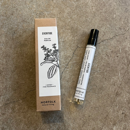 Norfolk Natural Living perfume box laying next to a 10ml tube of perfume called Eventide. The bottle is covered in a black and white label with a black lid on a grey concrete background