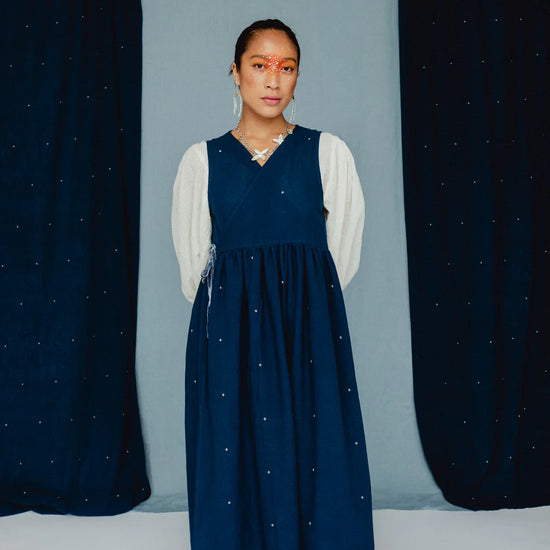Woman wearing a blue dress with white embroidered posies against a blue backdrop