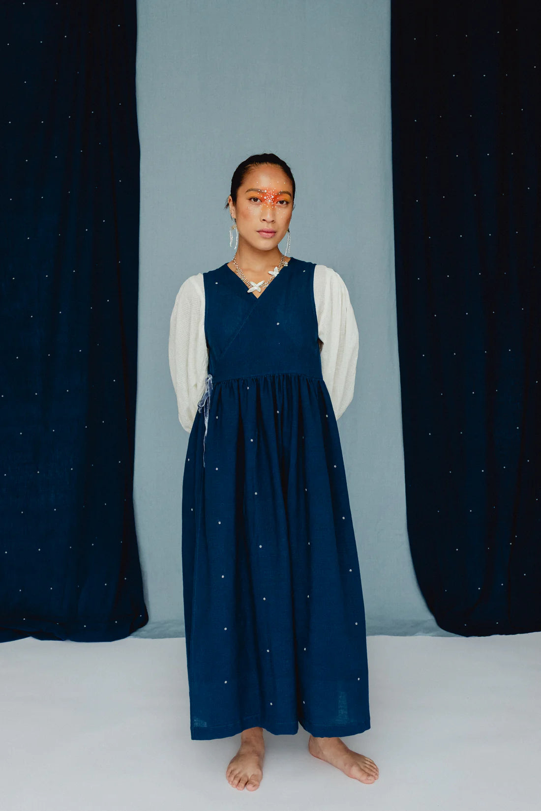 Woman wearing a blue dress with white embroidered posies against a blue backdrop