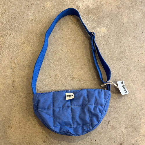 Cornflower blue cotton padded cross body bag with adjustable strap and zip on grey concrete background