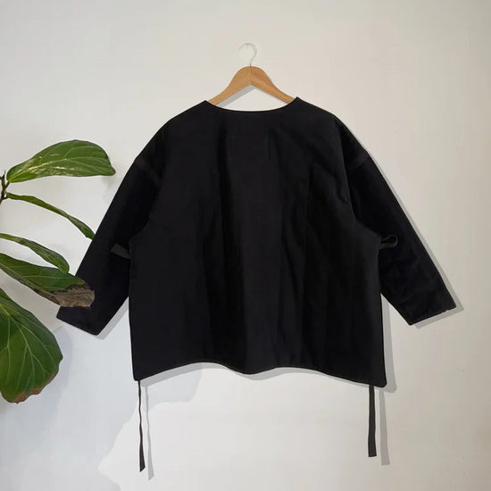 Black padded jacket on a hanger against a white wall with a plant in the corner